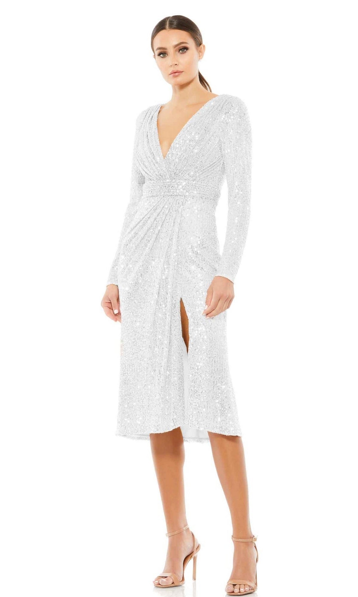 A woman wears the Mac Duggal 26555 long sleeve sequin party dress with a deep V-neck and front slit, paired with strappy high-heeled sandals, standing against a plain white background.